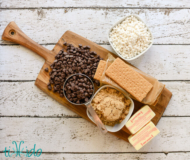 Ingredients for S'mores Toffee recipe on a wooden cutting board on a white wooden table.