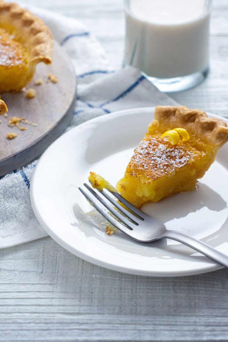 Slice of lemon chess pie on a white dessert plate with a silver fork.