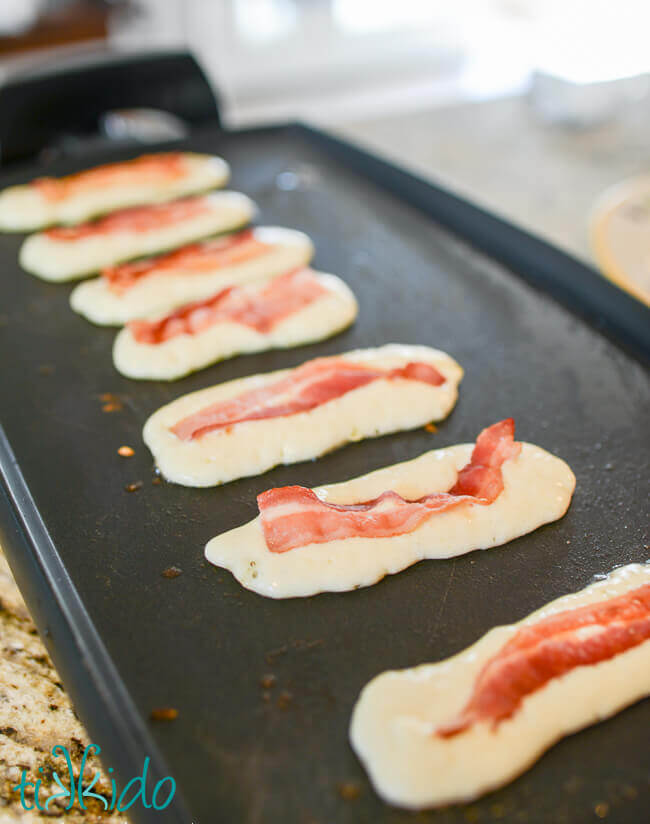 Bacon pancakes cooking on an electric griddle.