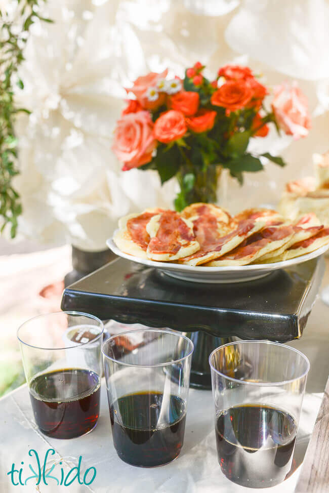 Bacon pancakes on a white plate next to clear glasses with real maple syrup for dipping.