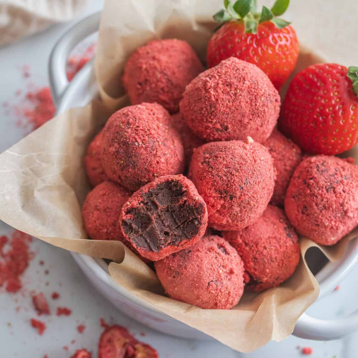 Bowl of chocolate covered strawberry truffles.  One truffle has a a bite taken out of it, showing the dark chocolate interior.