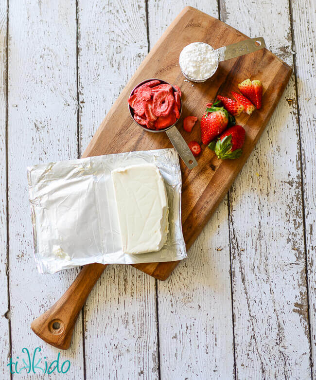 Ingredients for strawberry cream cheese on a wooden cutting board on a white weathered wood background