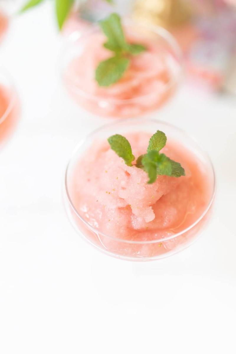 Light pink strawberry frose (frozen strawberry and rose wine cocktail), in two  champagne coupe glasses, garnished with sprigs of fresh mint. 