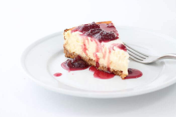 Pino strawberry reduction ice cream topping on top of cheesecake on a white plate.