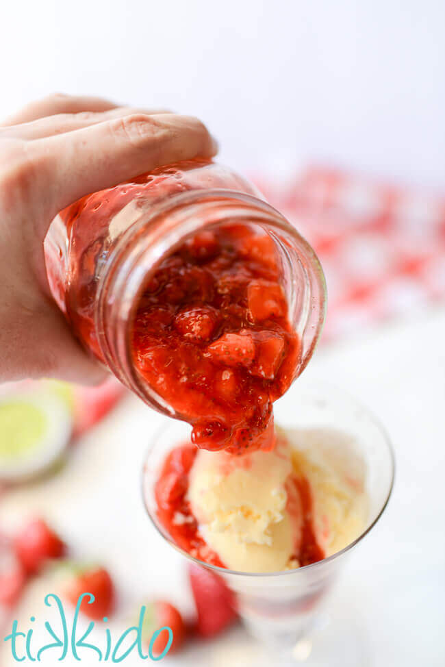 Homemade strawberry sauce being poured over vanilla ice cream.