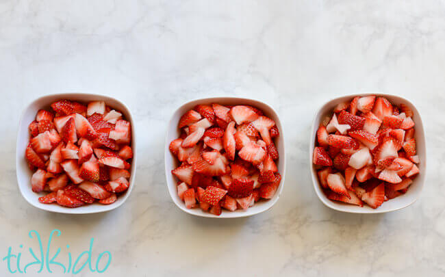 Fresh strawberries chopped and in three white bowls.