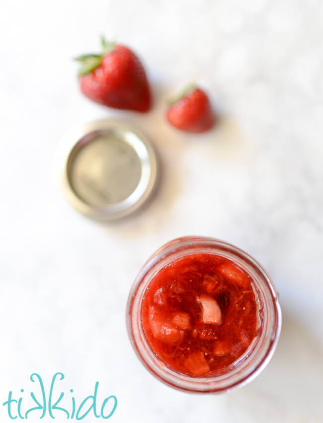Homemade strawberry sauce ice cream topping in a glass jar on a white background.