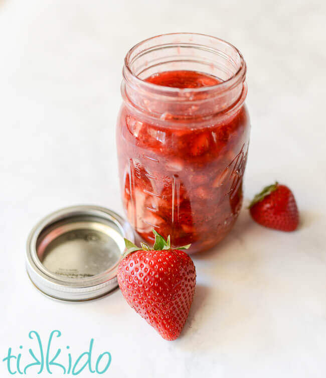 Homemade strawberry sauce ice cream topping in a mason jar, surrounded by fresh strawberries.