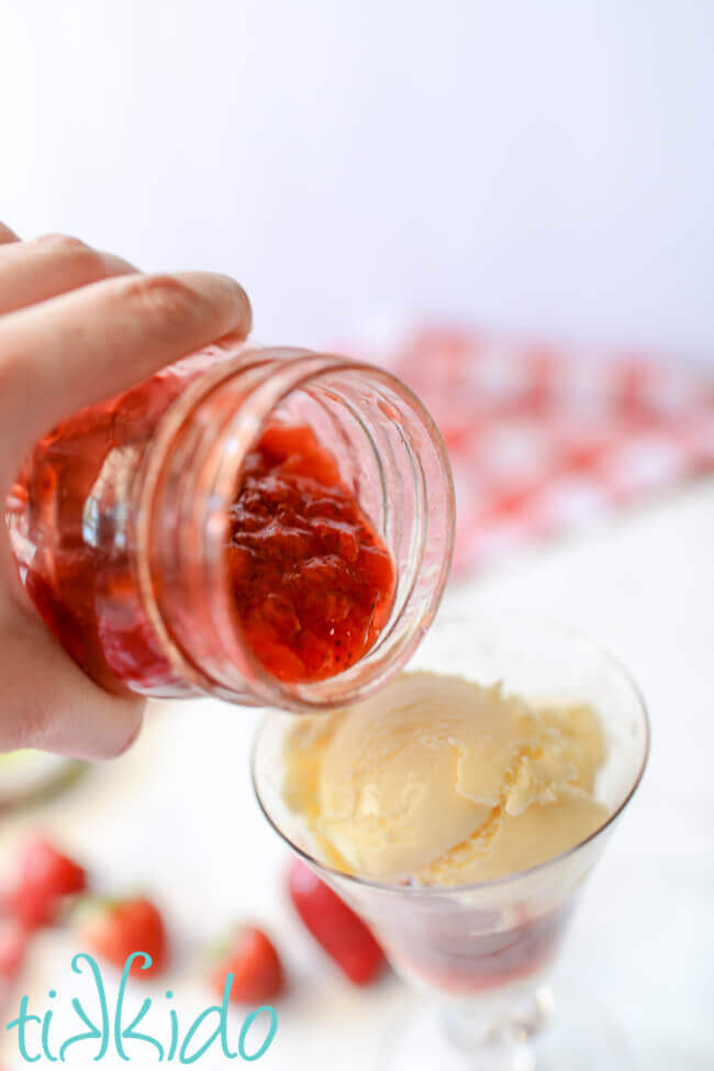 Homemade Strawberry Sauce being poured over vanilla ice cream.