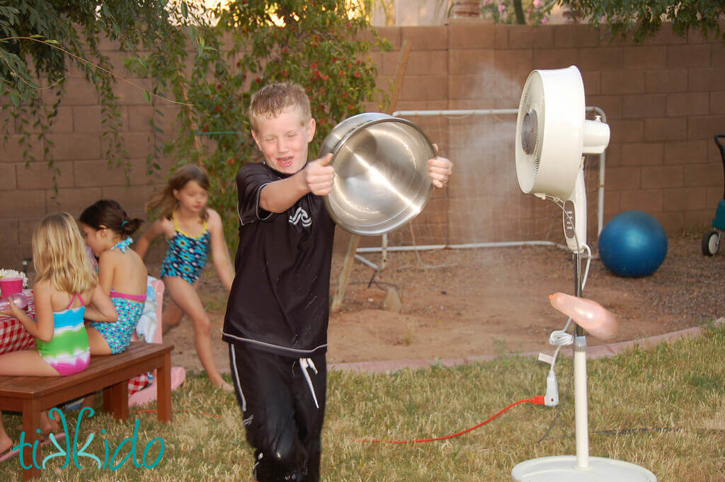 Little boy throwing a water balloon from a silver bowl.