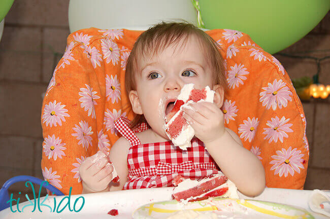 One year old eating a piece of strawberry cake at the Strawberry Picnic first birthday.