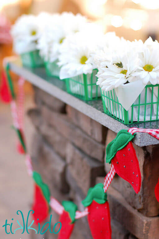 White flowers in green plastic strawberry baskets above a felt strawberry garland.