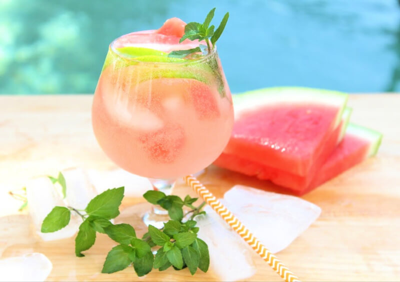 Watermelon mojito cocktail garnished with fresh lime, mint, and slices of watermelon, on a table in front of a pool.