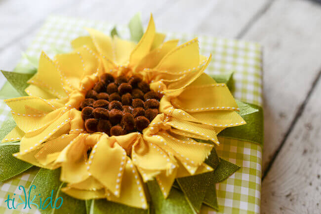 DIY ribbon sunflower gift topper on a green gingham check wrapped gift.