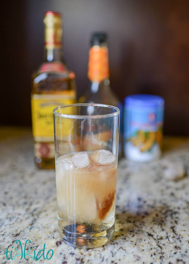 Tamarind margarita ingredients in a tall glass, bottles of the ingredients in background.