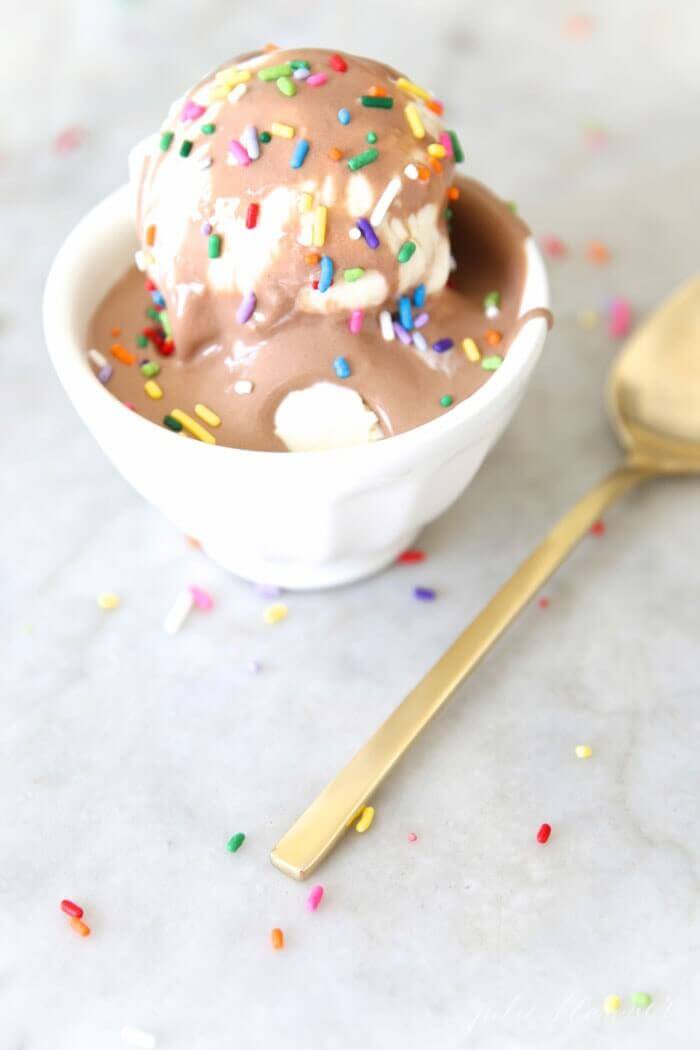 Chocolate marshmallow ice cream sauce over vanilla ice cream in a white bowl, topped with rainbow sprinkles.