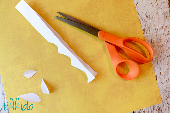 Small paper leafs being cut out of a piece of folded white paper.