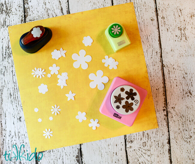 paper flower shapes cut out of white paper with paper punches on a sheet of yellow paper.