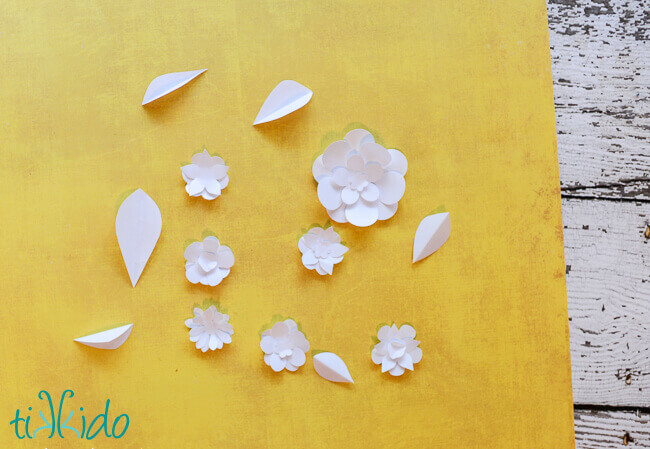 Small white paper flowers on a piece of yellow scrapbook paper.