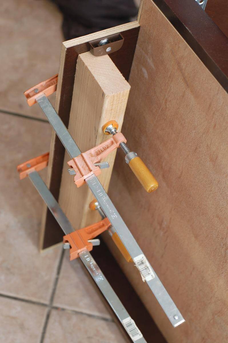 Brace being screwed to underside of cabinet to make hidden toe kick drawers.