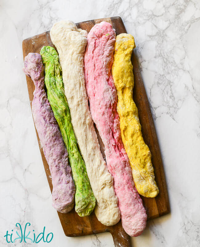 purple, gree, white, pink, and yellow ropes of bagel dough ready to form rainbow unicorn bagels.