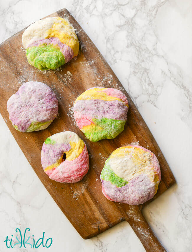 Rainbow bagel dough divided into bagel sized pieces on a wooden cutting board.