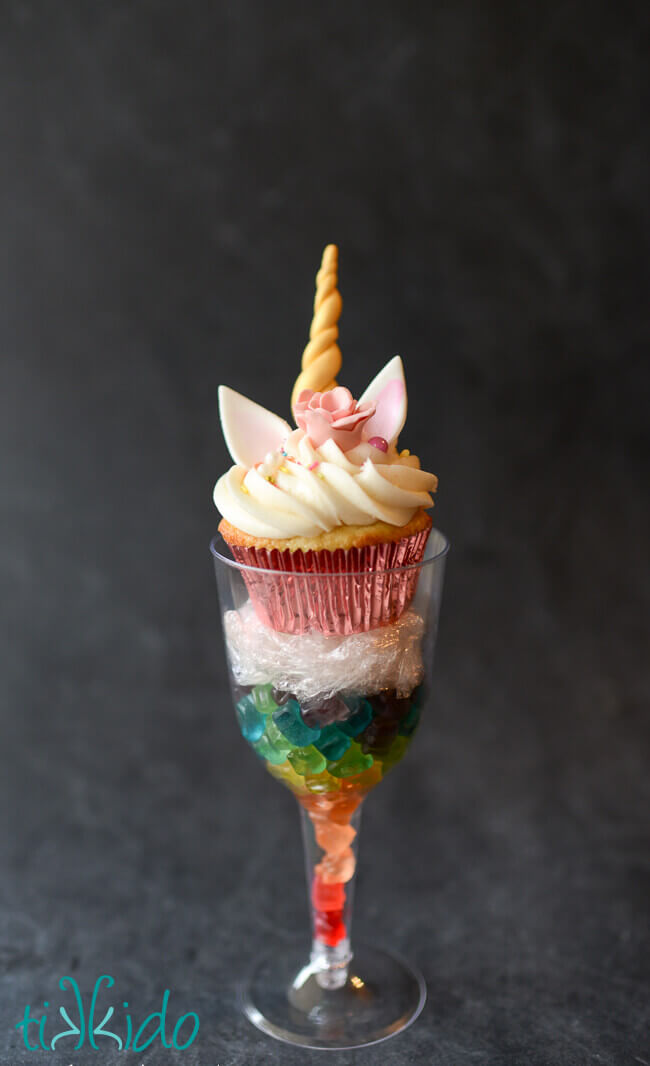 Unicorn cupcake displayed in a disposable plastic wine glass filled with a rainbow of miniature gummy bears.