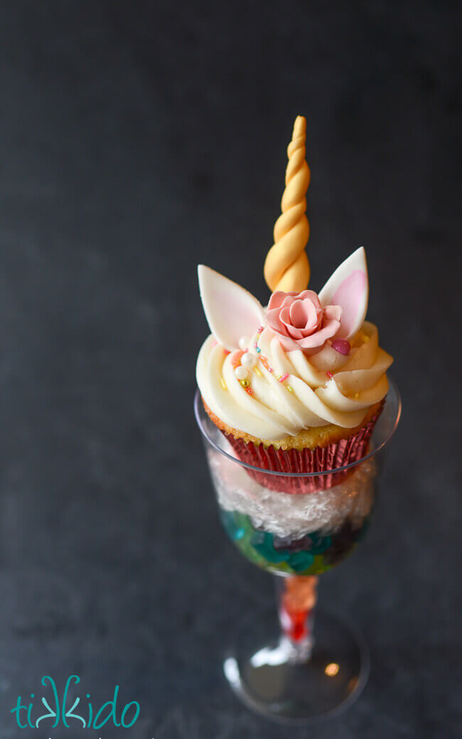 Unicorn cupcake displayed in a disposable plastic wine glass filled with a rainbow of miniature gummy bears.