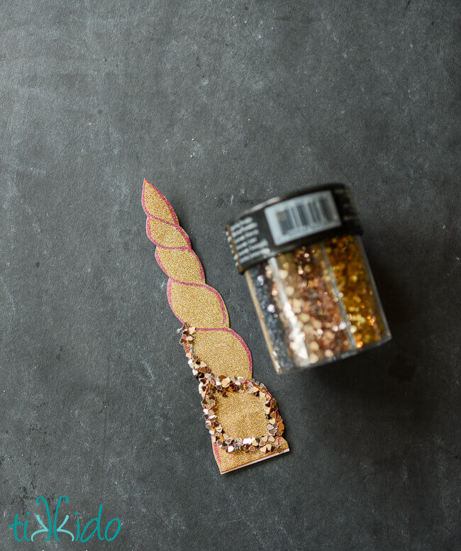 Glitter outline being glued on a sparkly gold paper unicorn horn for the unicorn party favor bag.