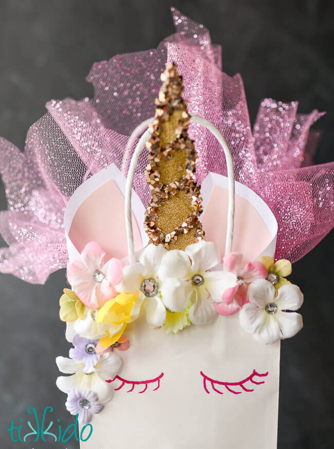 Close up of the DIY unicorn party favor bag, with a golden glittery horn, silk flower and rhinestone mane, paper ears, and glittery tulle inside the bag.