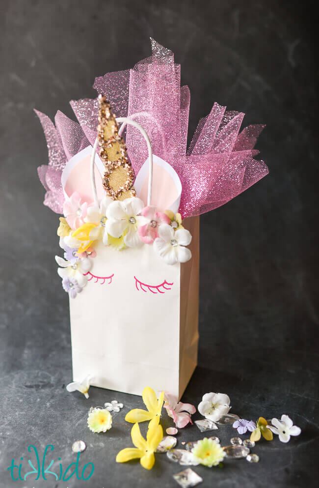 Unicorn Party Favor Bag made from a plain white paper gift bag, featuring a glittery golden horn, silk flower and rhinestone mane, and glitter tulle instead of tissue paper.