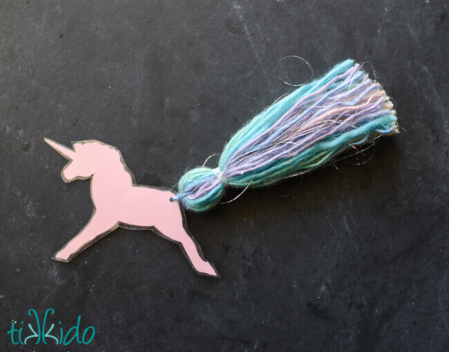 Unicorn bookmark with a yarn tassel tail on a black chalkboard background.