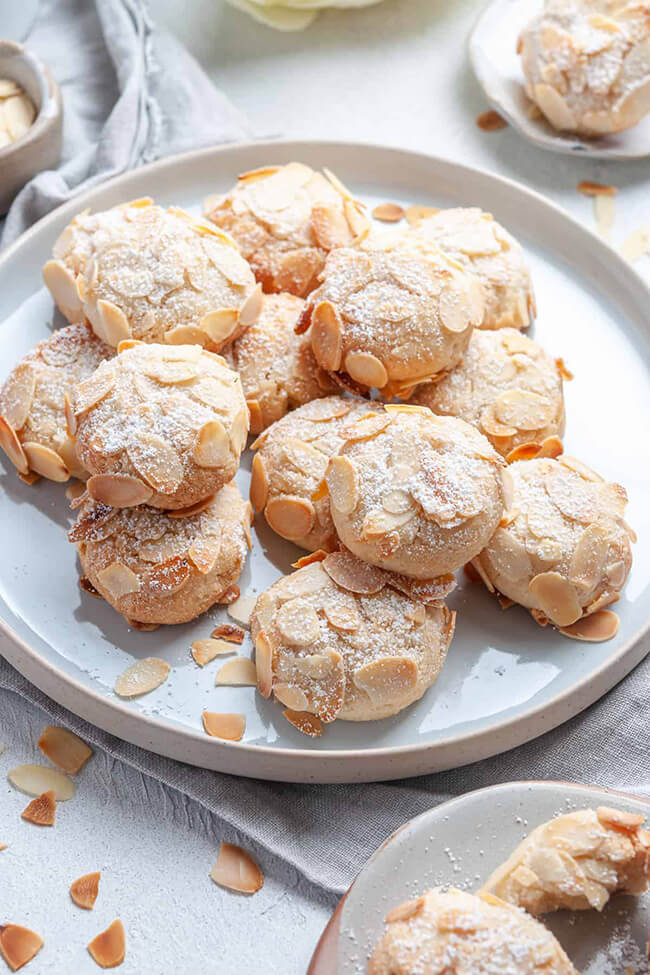 Vegan almond cookies sprinkled with powdered sugar on a white plate.