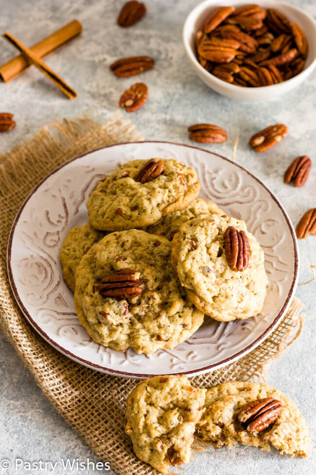 Vegan pecan cookies on a plate, surrounded by whole pecans and cinnamon sticks.