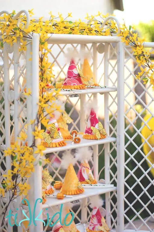 White cane display cabinet filled with pink and yellow party hats and ribbon wands.