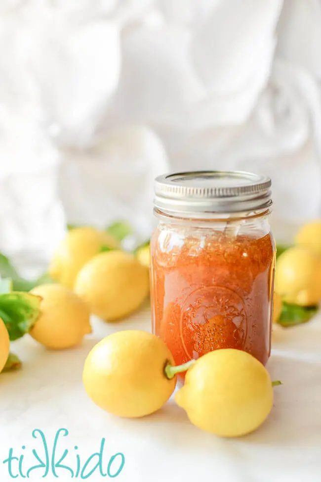 Jar of lemon jam surrounded by whole lemons.