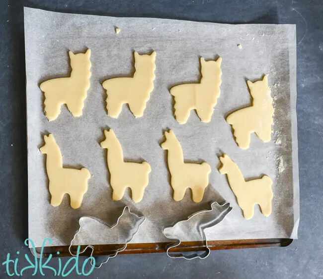 Cookie dough cut into eight llama shapes on a parchment lined cookie sheet.