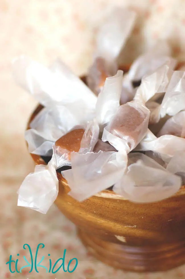 Wooden bowl filled with homemade salted caramel candies wrapped in waxed paper.