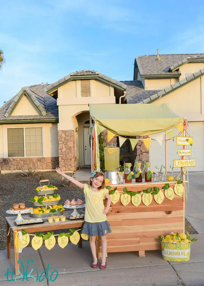 Little girl standing in front of a lemonade stand.