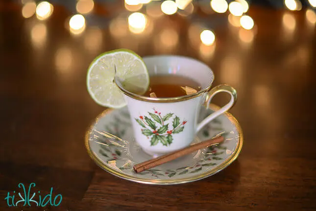 Christmas mug filled with mulled cider, with a slice of lime on the edge of the mug and christmas lights in the background.