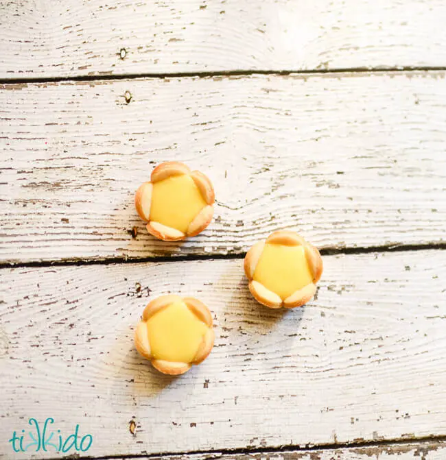 Three miniature lemon tartlets that look like flowers on a white wooden surface.