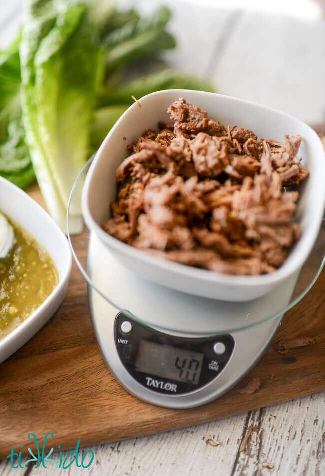 Mexican shredded beef in a white bowl on a kitchen scale reading 4 ounces.