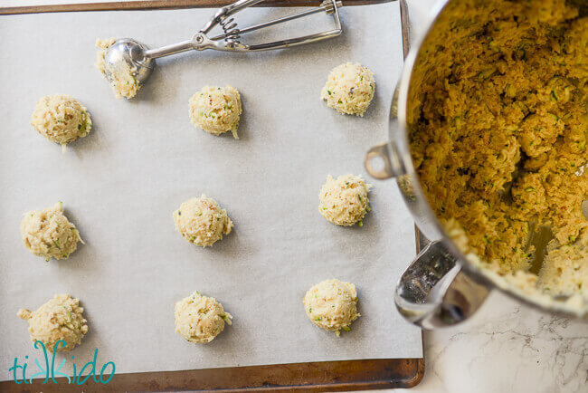 Zucchini cookie dough being scooped on a parchment lined cookie sheet.